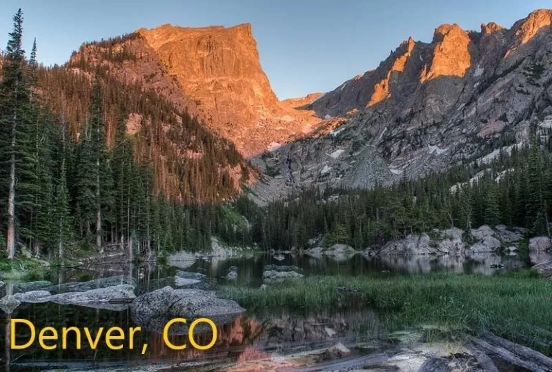 A mountain range with trees and water in the foreground.